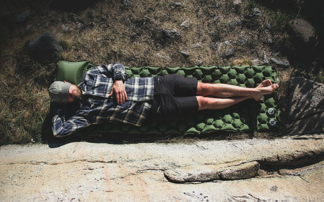 Person lying on a sleeping pad outdoors, surrounded by natural rocky terrain.